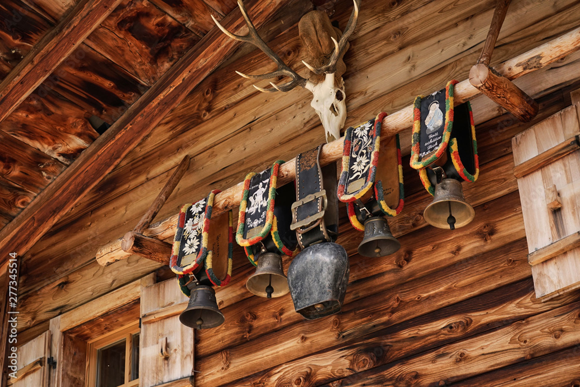 Almhütte mit traditionellen Kuhglocken am Band an Hauswand von Holzhütte unter Hirschschädel