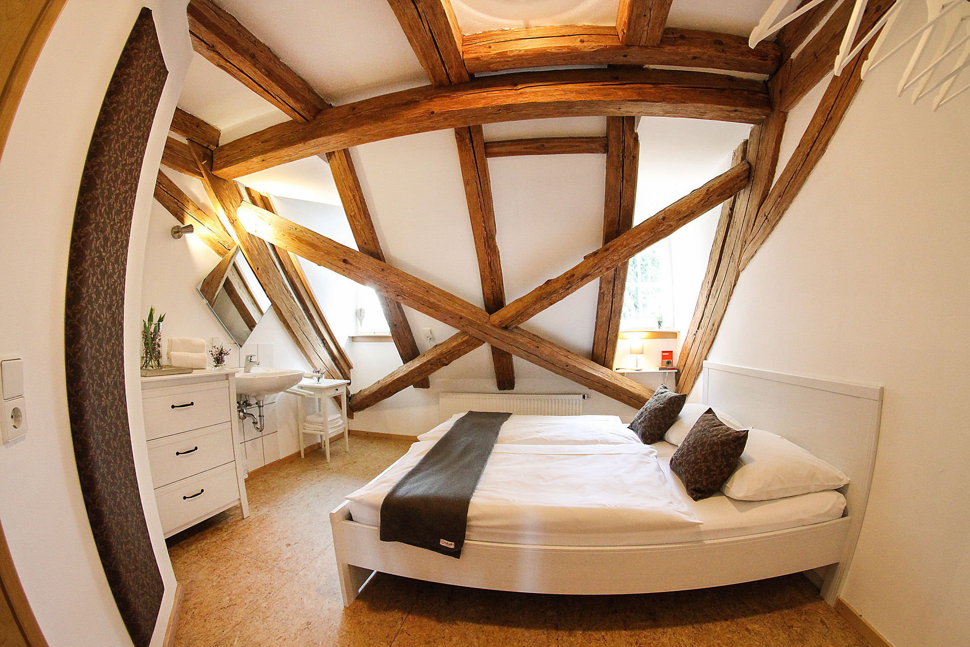 Doppelbett in Dachzimmer Gasthaus Einkorn. Dachbalken, weiße Wände, zwei Fenster, helle Atmosphäre