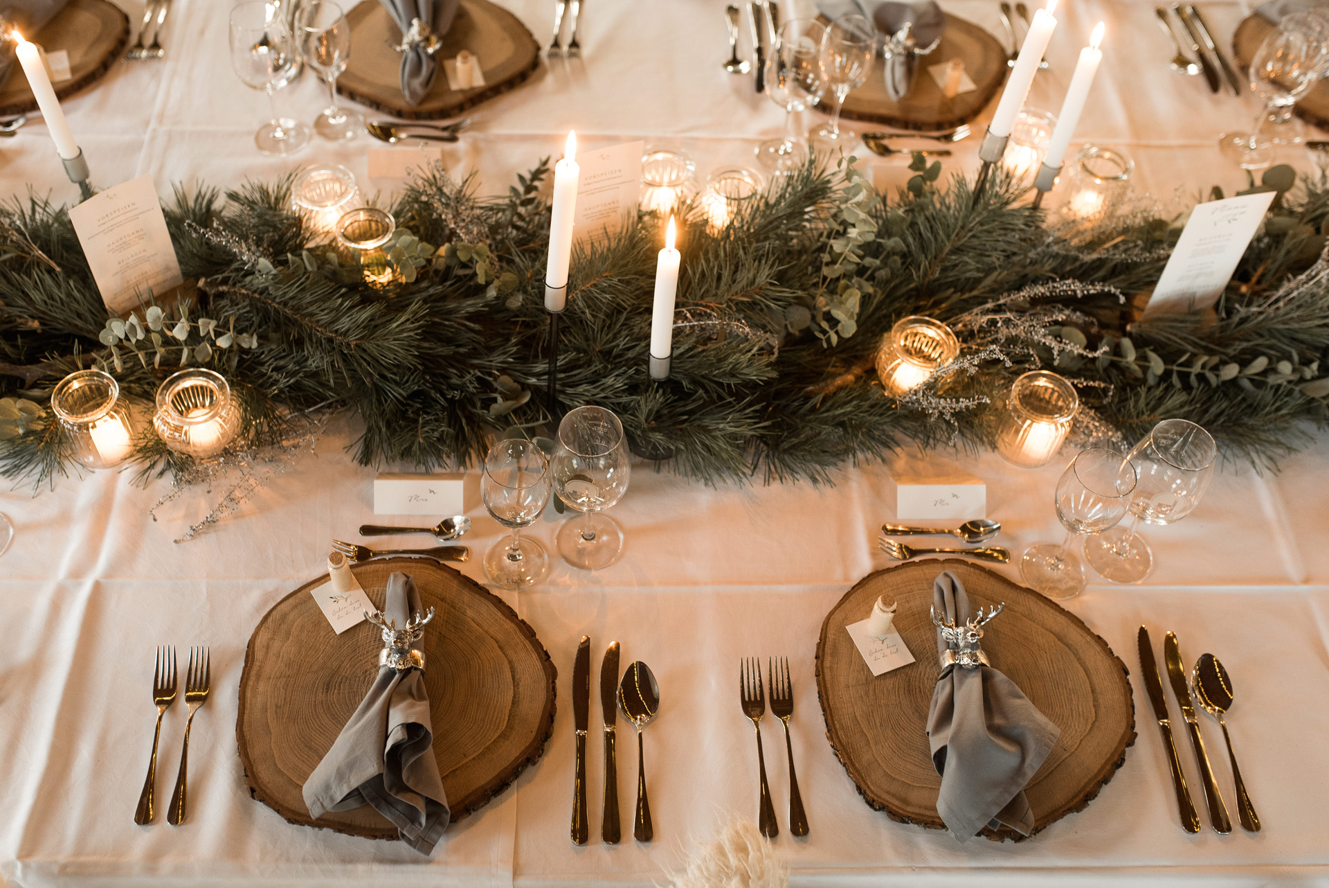 Winterliche Hochzeitstafel Holzplatten, Servietten mit Hirschkopfring, Silberbesteck, Kerzen und Zweige